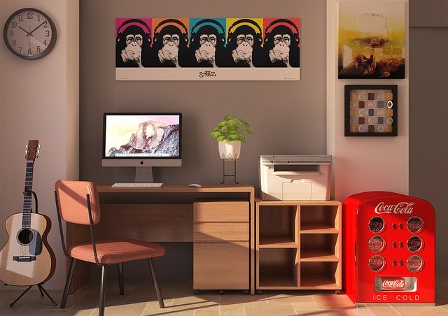 kancelář v domácím prostředí, stůl, židle, počítač, tiskárna, obrázky opice různě barevné, kytara, hodiny kulaté na stěně, zařízení coca-cola